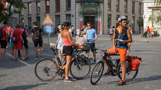 Cyclists stand next to Ljubljana's special weather zone, marked by a yellow sign.